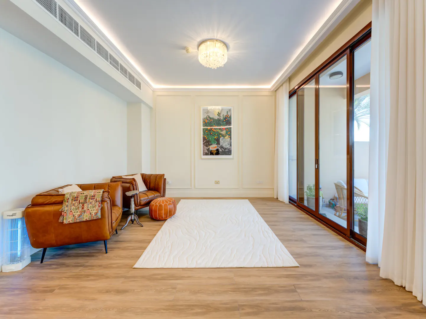 Living room with brown leather chairs, white rug, and sliding glass doors to a patio. A colorful painting hangs on the wall.