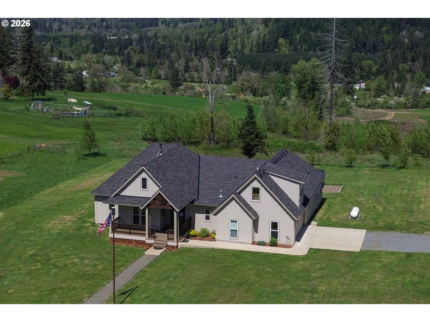 Aerial view of a beige single-story house with a dark gray roof, green lawn, and wooded hills in the background.