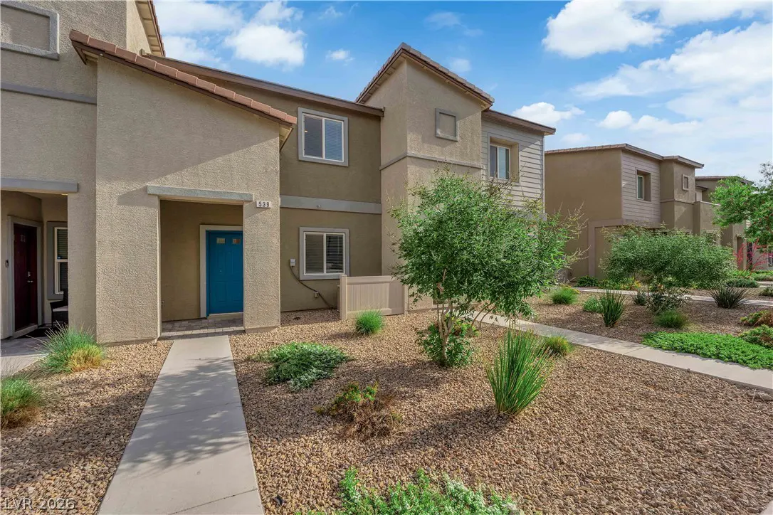 Tan two-story townhouses with a blue door and brown rock landscaping under a blue sky.