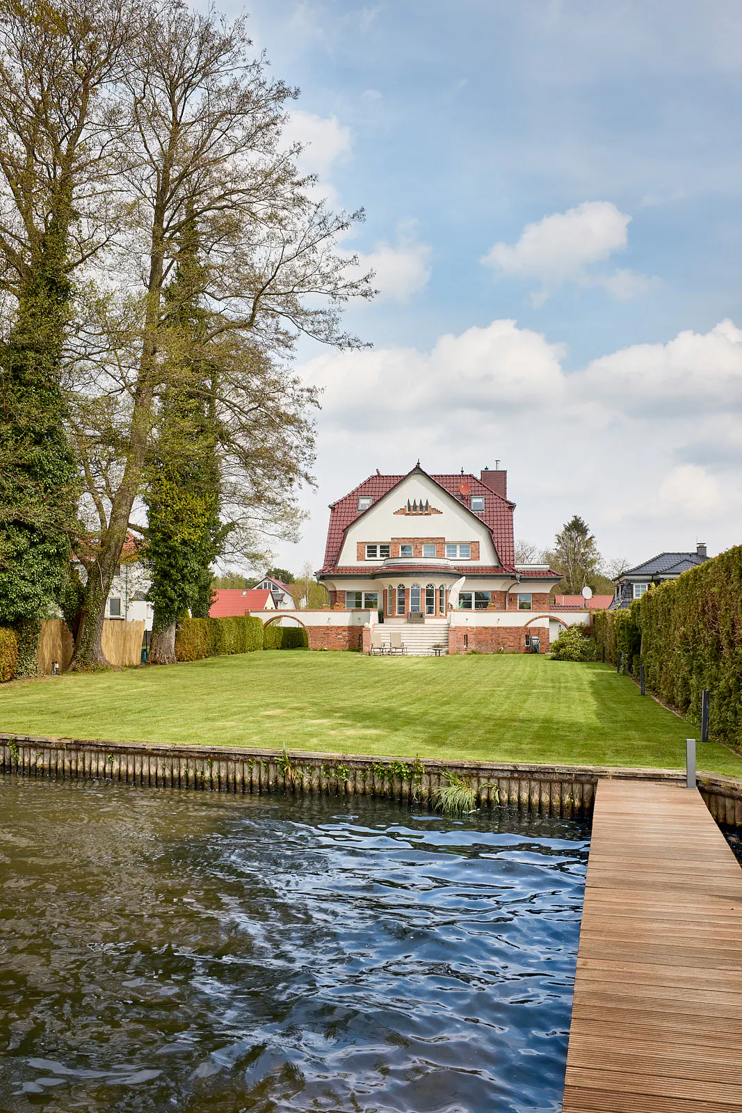 Waterfront property with a large lawn, a dock, and a white house with a red roof in the background.