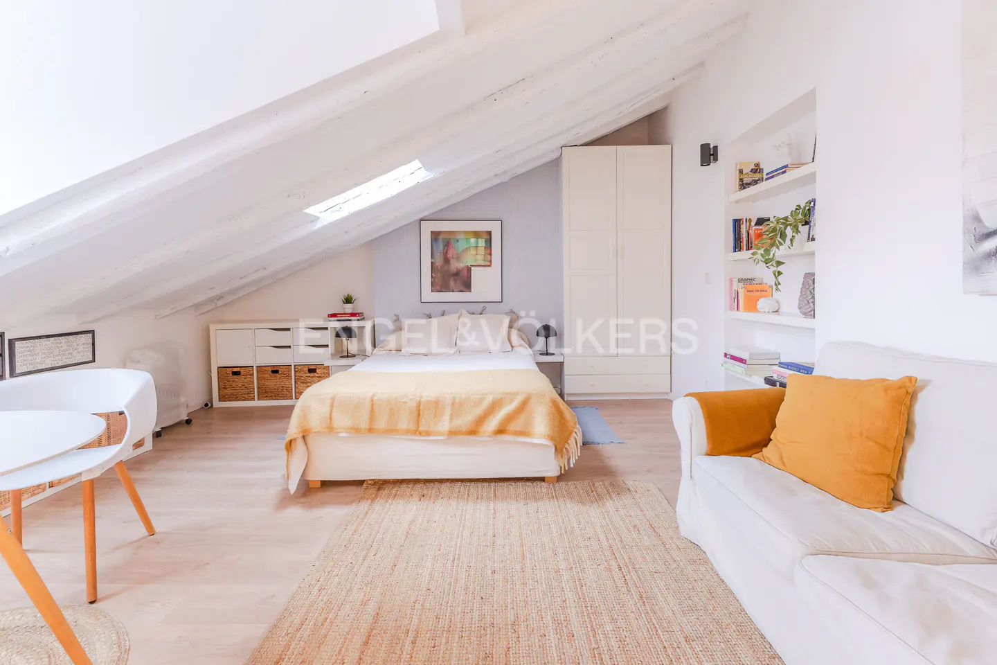 Bright, airy attic bedroom with white walls, a bed with a yellow blanket, and a white sofa with a yellow pillow.