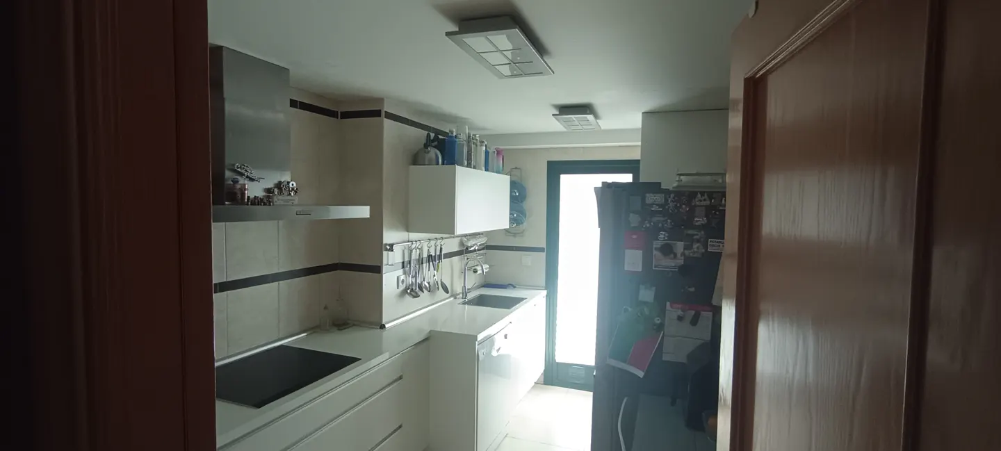 A galley kitchen with white cabinets, stainless steel appliances, and a black refrigerator. A door is visible on the right.
