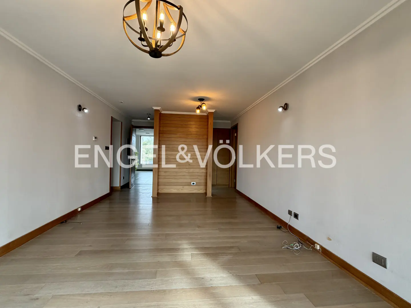 Wide shot of a bright, empty living room with light wood floors, white walls, and a rustic chandelier.