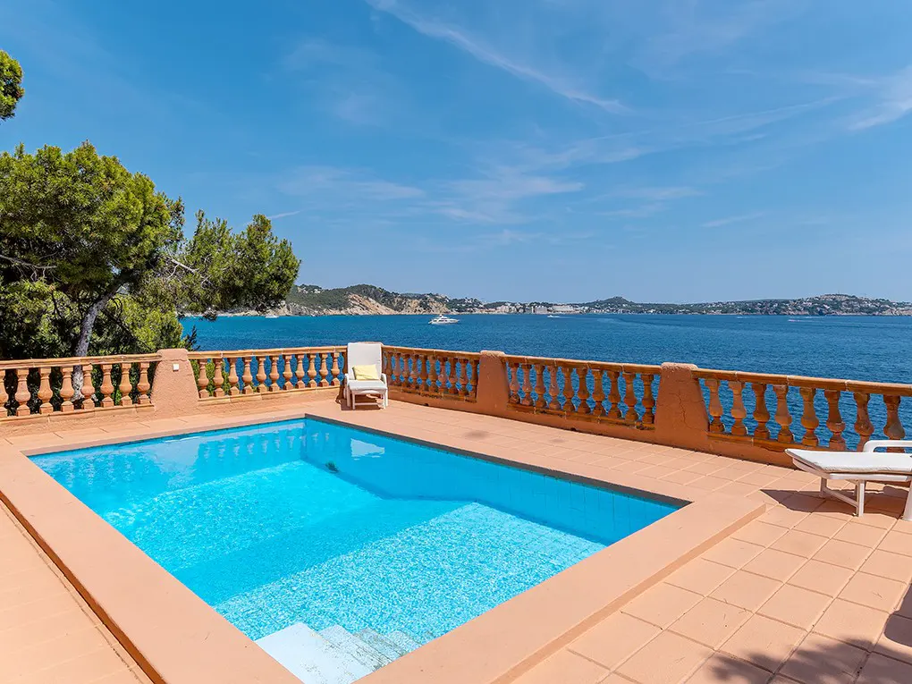 Outdoor pool with turquoise water and terracotta tile deck overlooking the ocean on a sunny day.