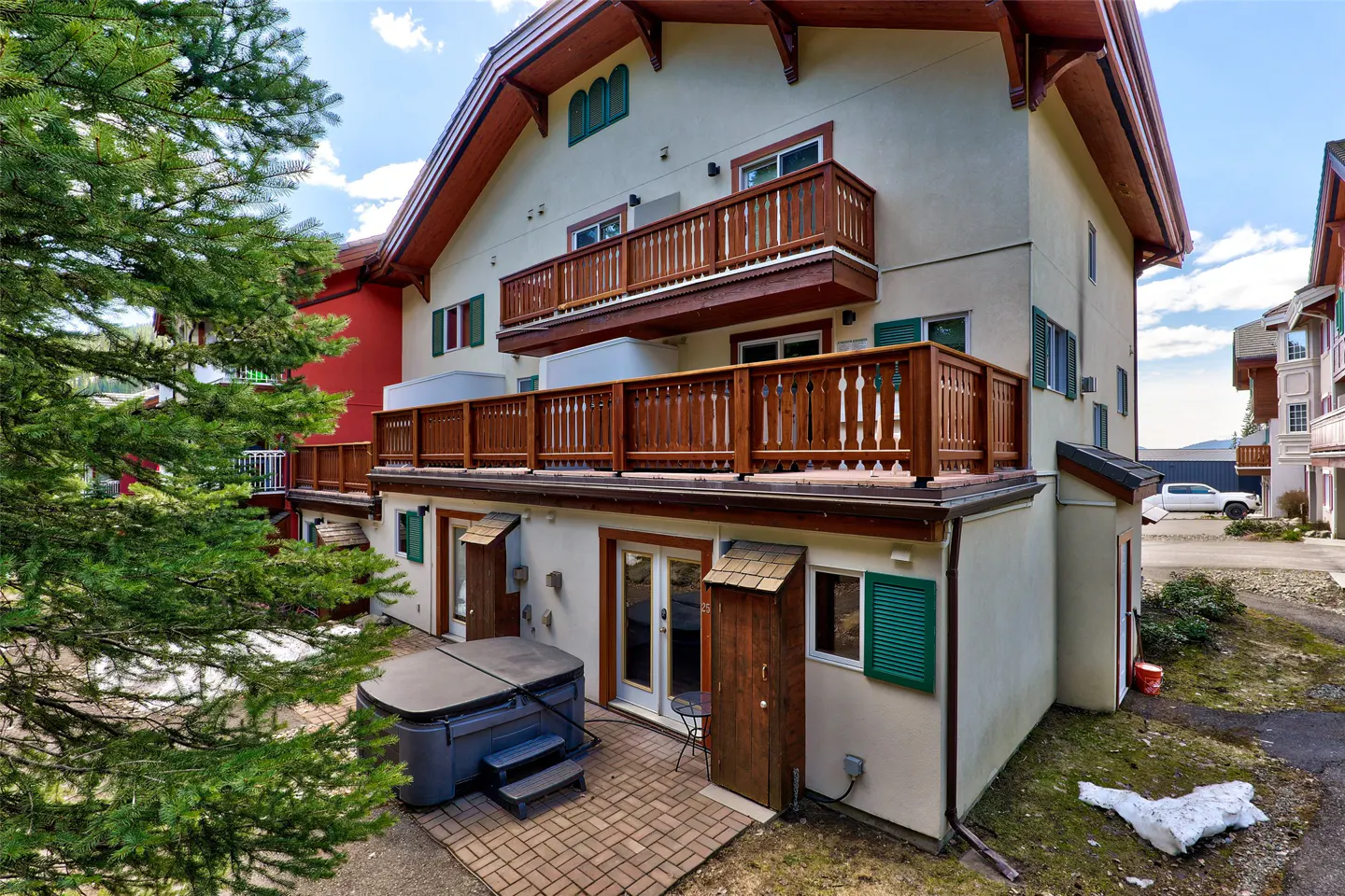 Exterior view of a multi-story building with balconies, a hot tub, and green shutters.
