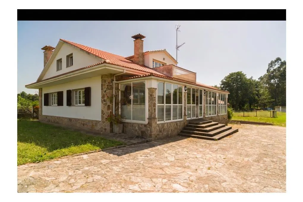 A two-story house with a red tile roof, stone accents, and a glass-enclosed porch.
