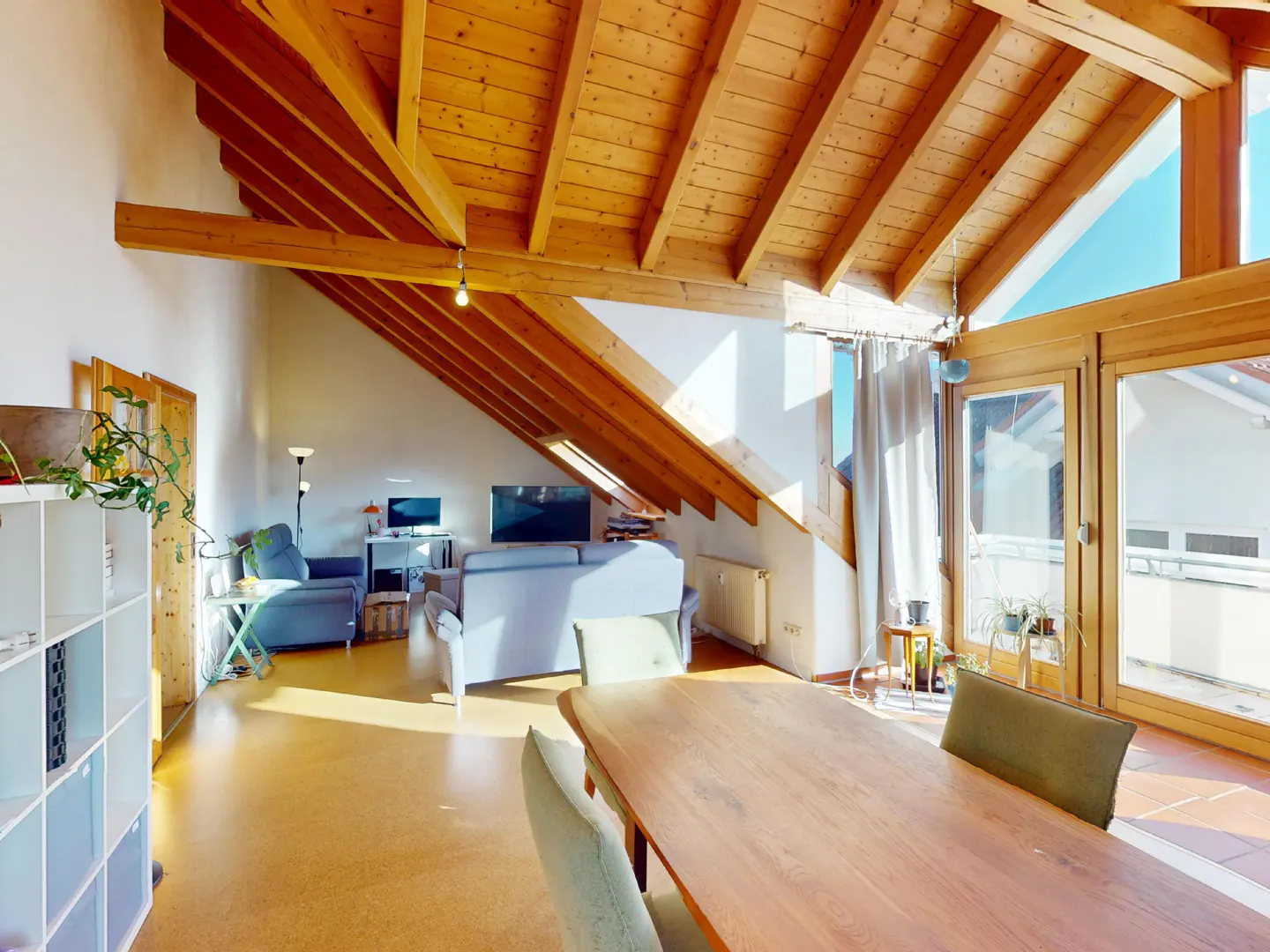 Bright living room with wood ceiling beams, a dining table, and a seating area with a blue sofa. Large windows let in natural light.