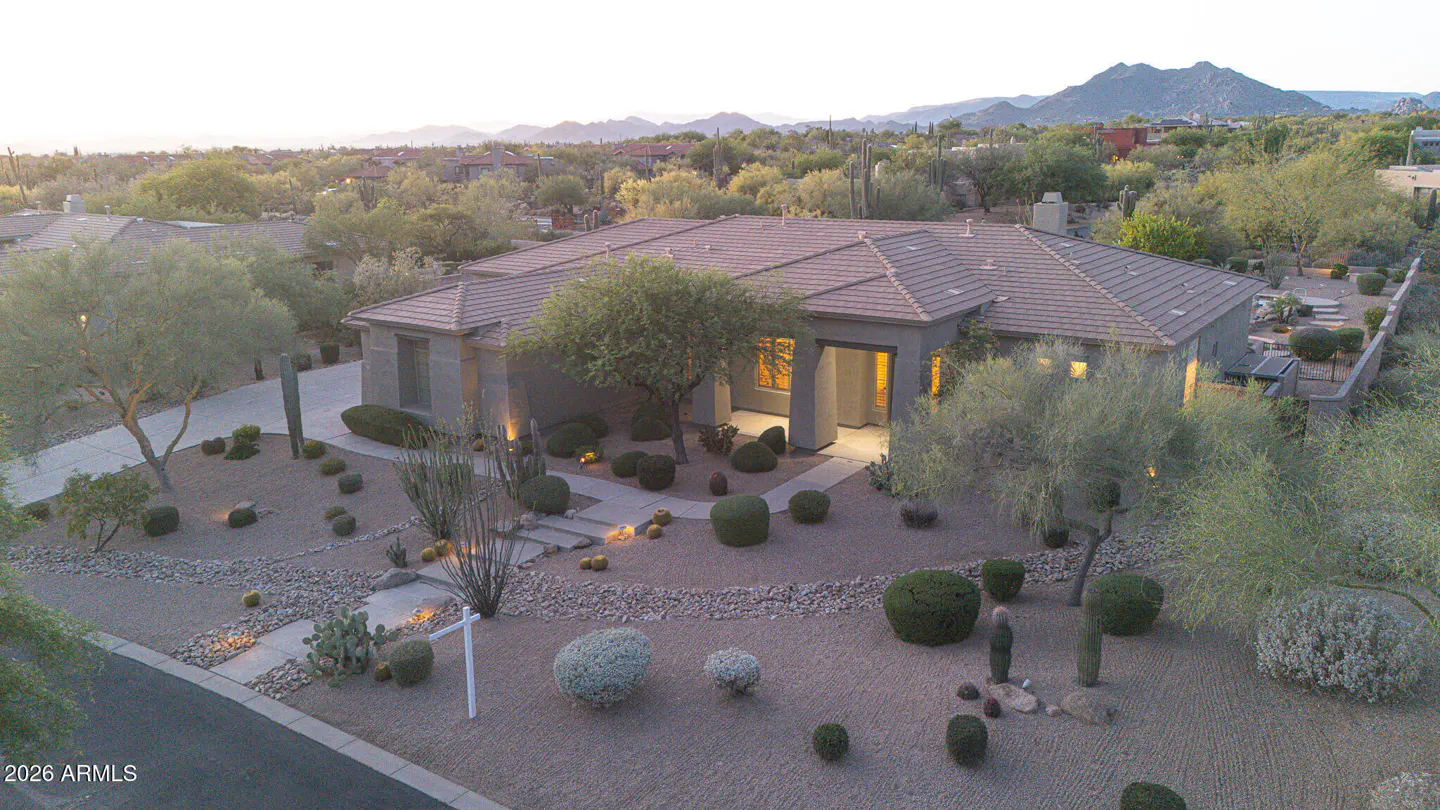 Aerial view of a tan single-story home with a brown tile roof, desert landscaping, and mountains in the background.