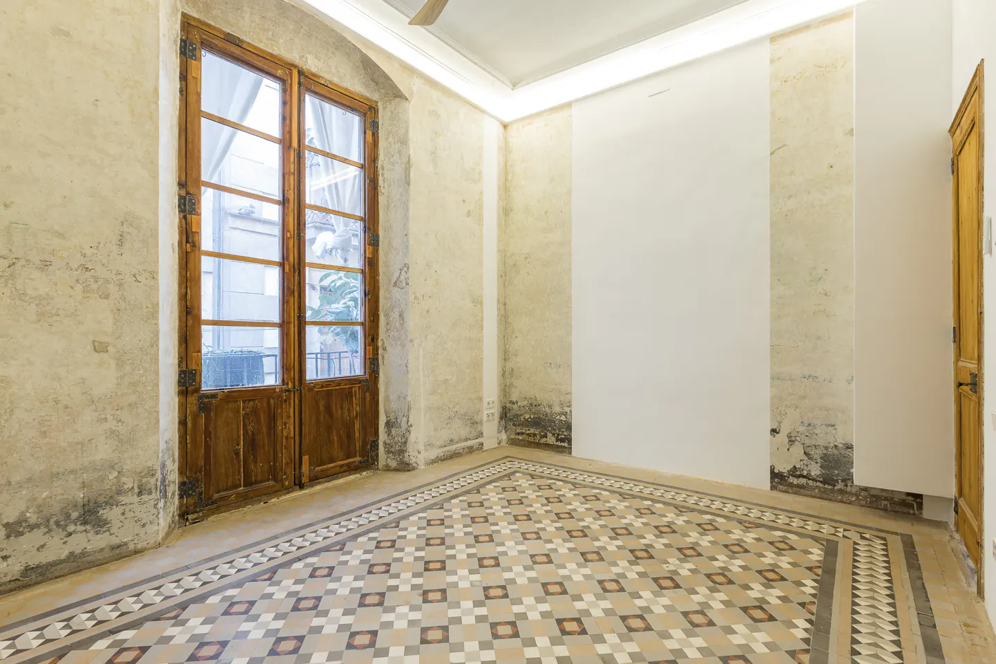 An empty room with a patterned tile floor, textured walls, and a large wooden window. A wooden door is visible on the right.