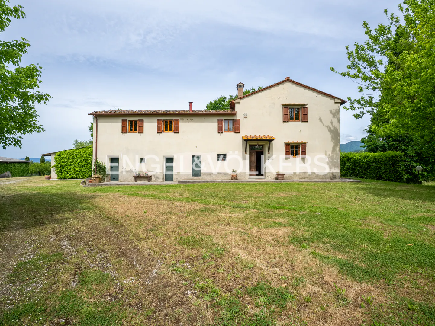 Two-story beige house with brown shutters and a green lawn on a sunny day.