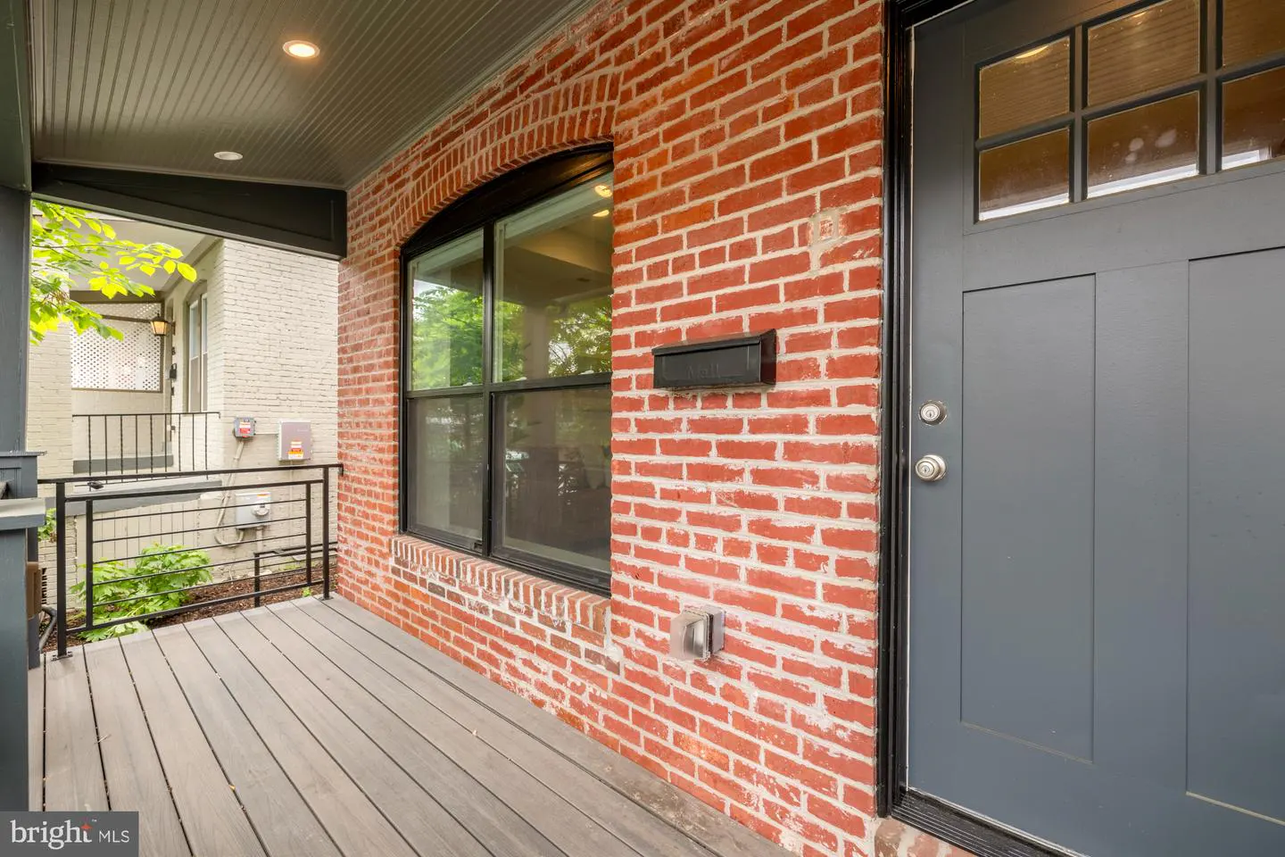 Exterior view of a red brick house with a gray front door and a small porch with gray wood flooring.