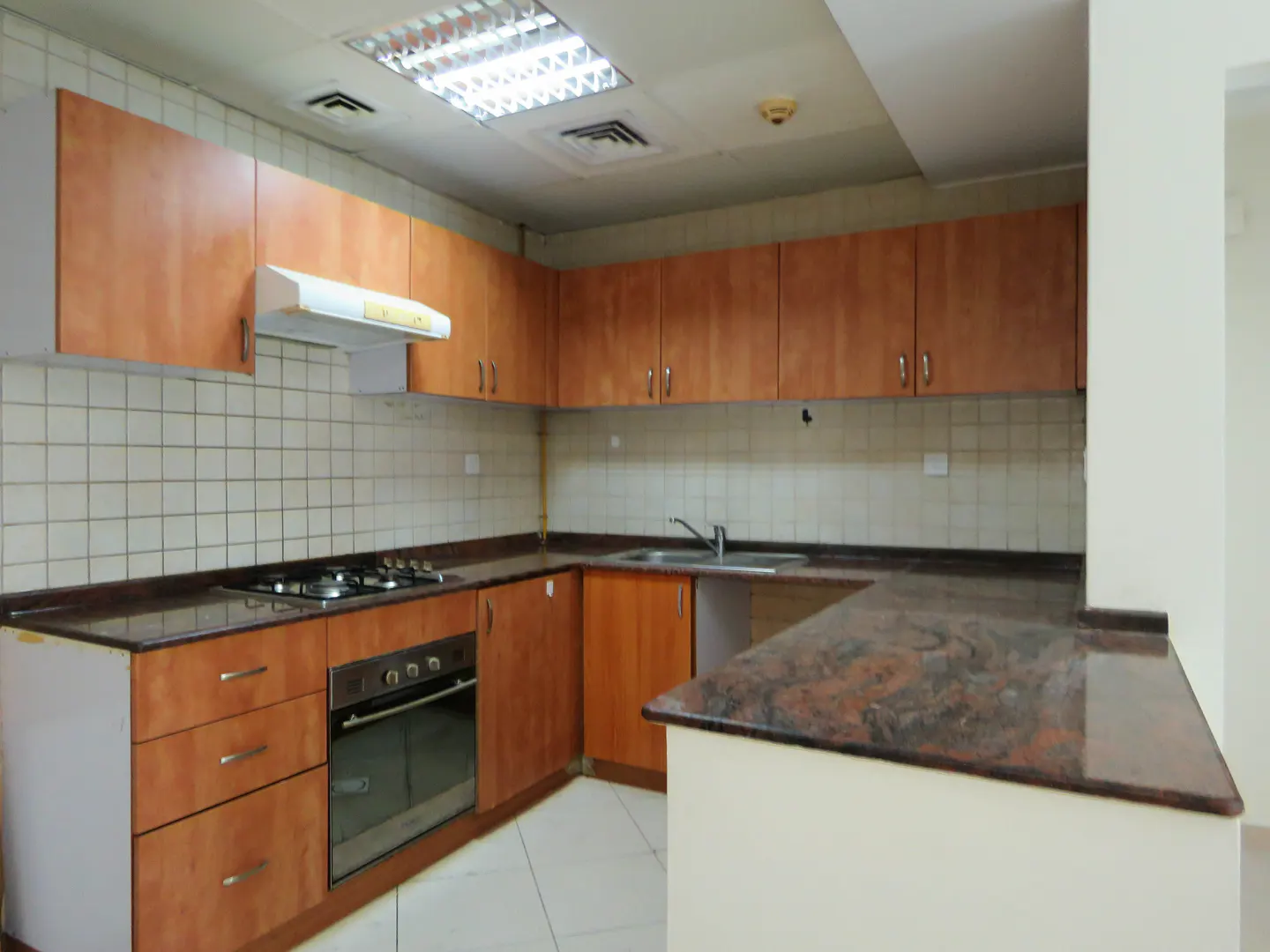 A kitchen with wood cabinets, brown granite countertops, a gas stove, and white tile flooring.