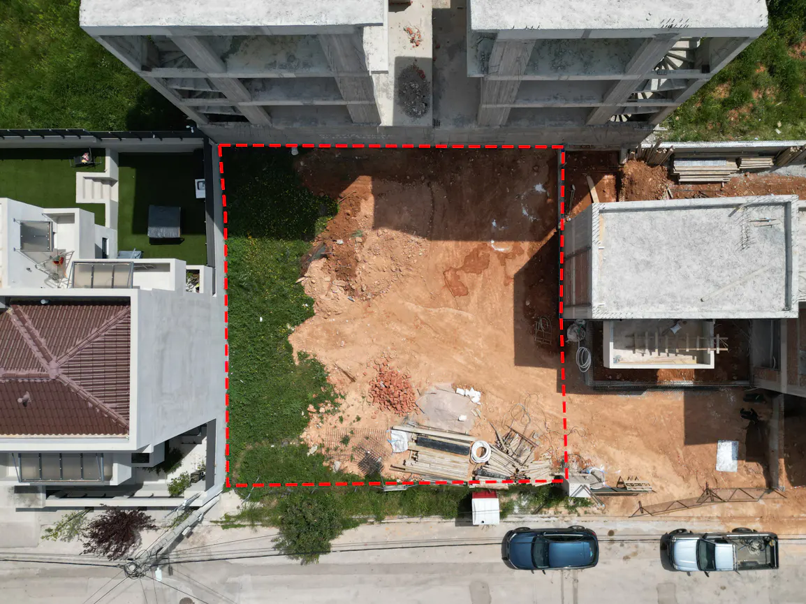 Aerial view of a vacant lot outlined in red, surrounded by buildings, grass, and a street with parked cars.