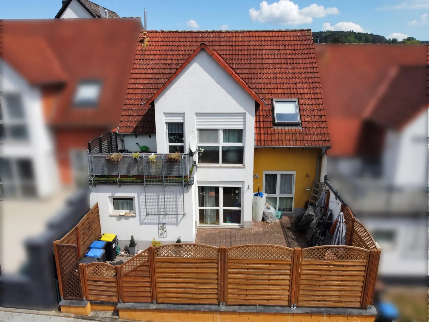 Aerial view of a two-story house with a red tile roof, white walls, and a wooden fence enclosing a small yard.