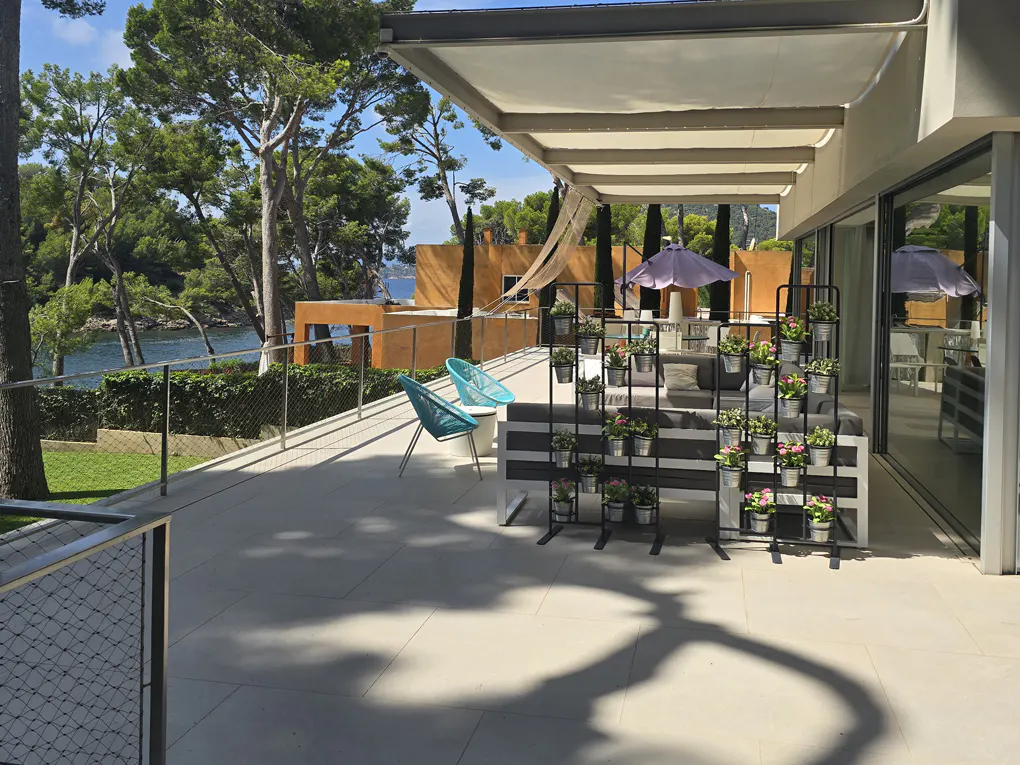 Spacious modern patio with outdoor seating, a vertical plant display, and a scenic view of the ocean and pine trees.