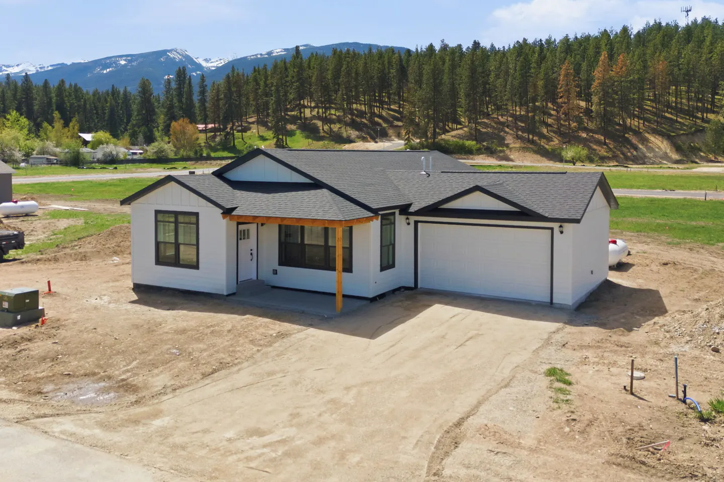 A modern white house with a gray roof and black trim, set against a backdrop of mountains and trees.