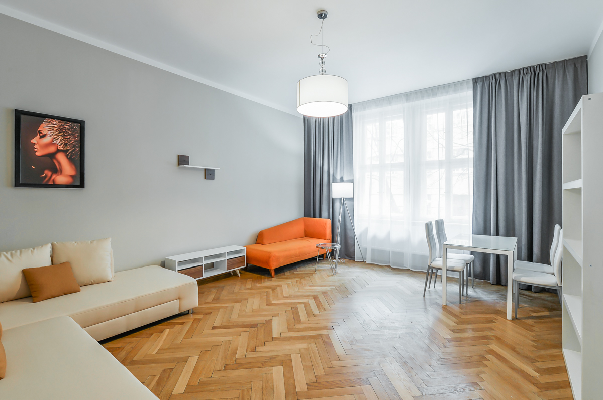 Modern living room with herringbone wood floors, beige sectional, orange chaise, dining set, and grey curtains. [AI-generated text]
