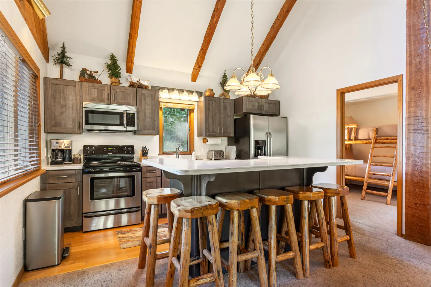 A kitchen with gray cabinets, stainless steel appliances, and a white countertop island with wooden stools.