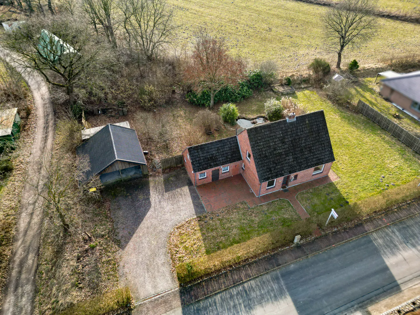 Aerial view of a red brick house with a dark roof, a detached garage, and green lawns in a rural setting.