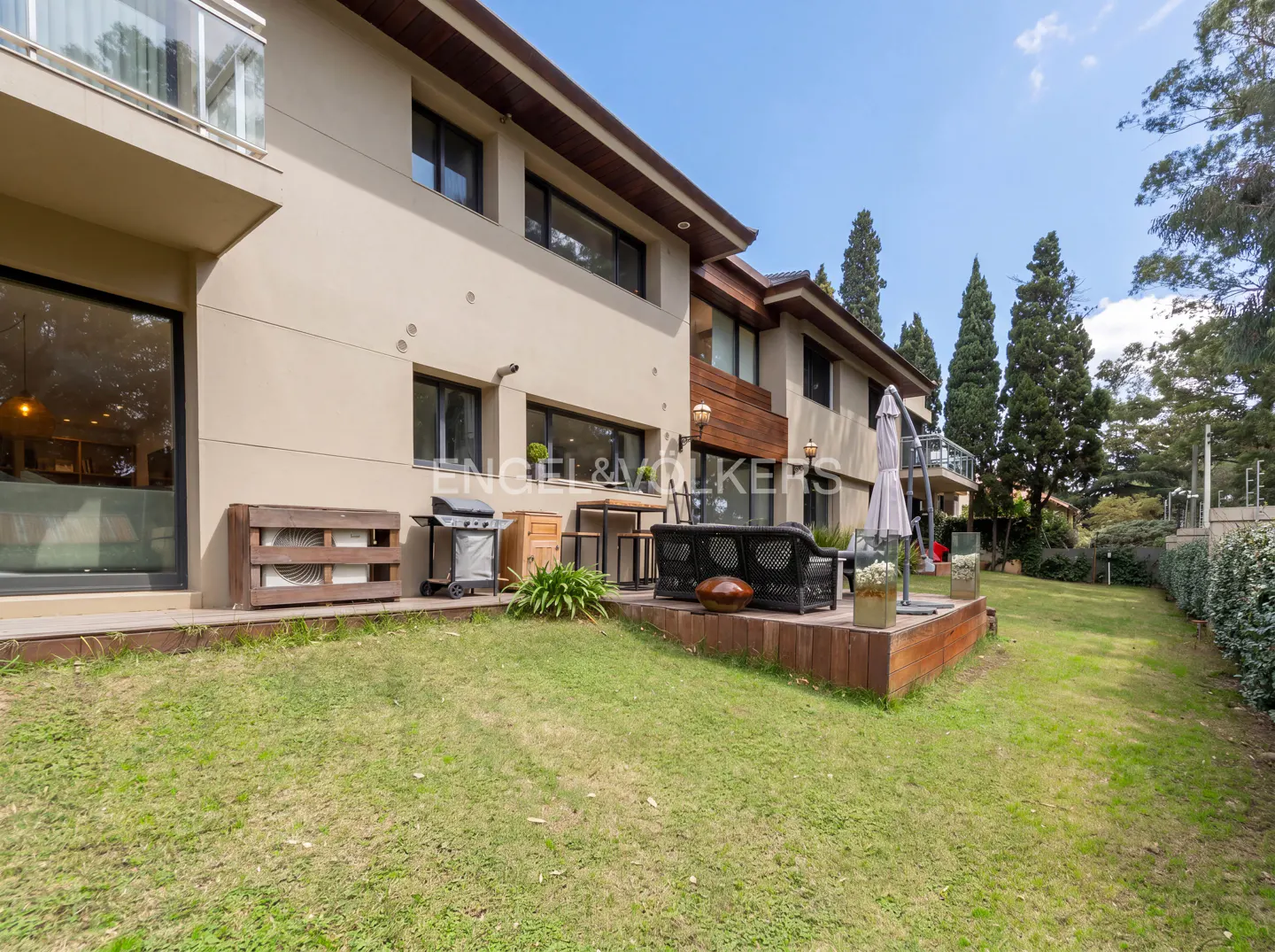 Backyard of a beige two-story house with a grill, patio furniture, and green lawn.