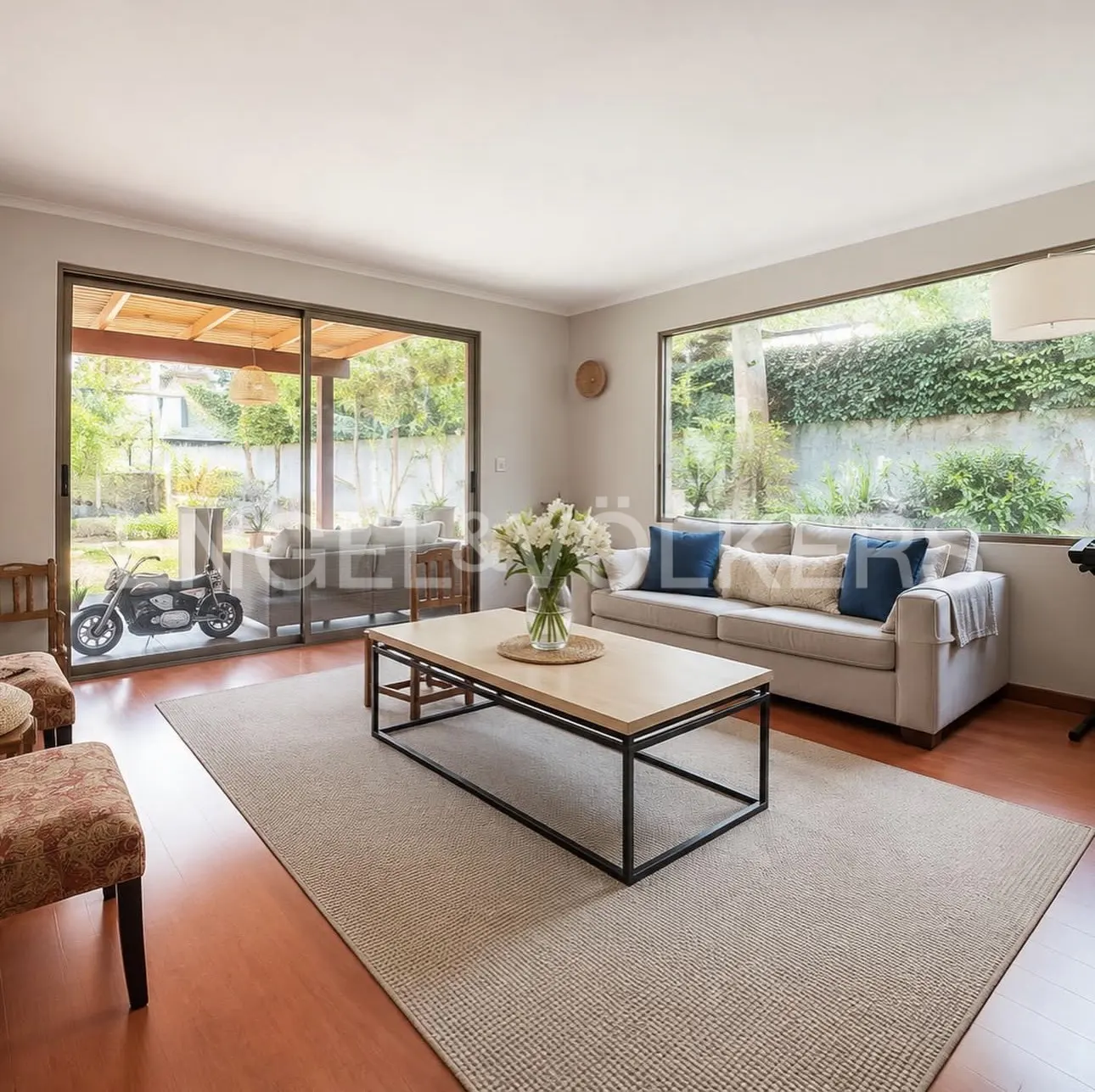 Living room with a gray sofa, a light wood and black metal coffee table with white flowers, and a motorcycle visible through sliding glass doors.