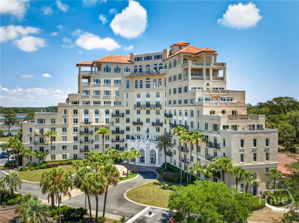 Exterior view of a large, multi-story beige building with a red tile roof, palm trees, and a circular driveway.