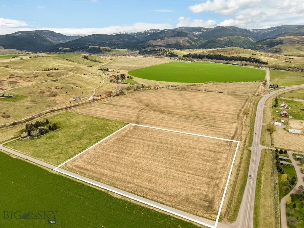 Aerial view of a large, rectangular plot of land outlined in white, surrounded by fields and mountains under a blue sky.