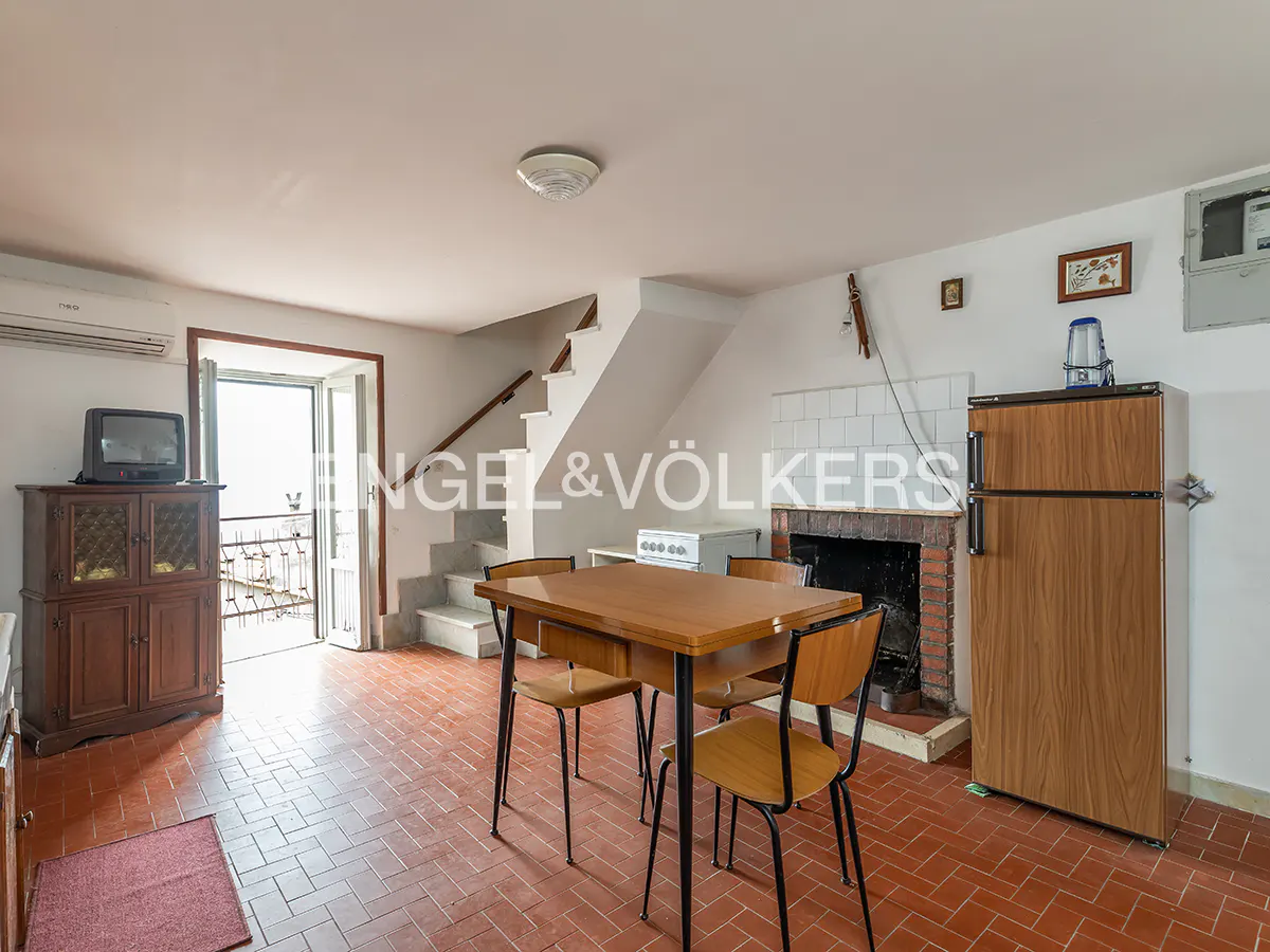 A kitchen with red tile floors, a wooden table with four chairs, a fireplace, and a wooden refrigerator.