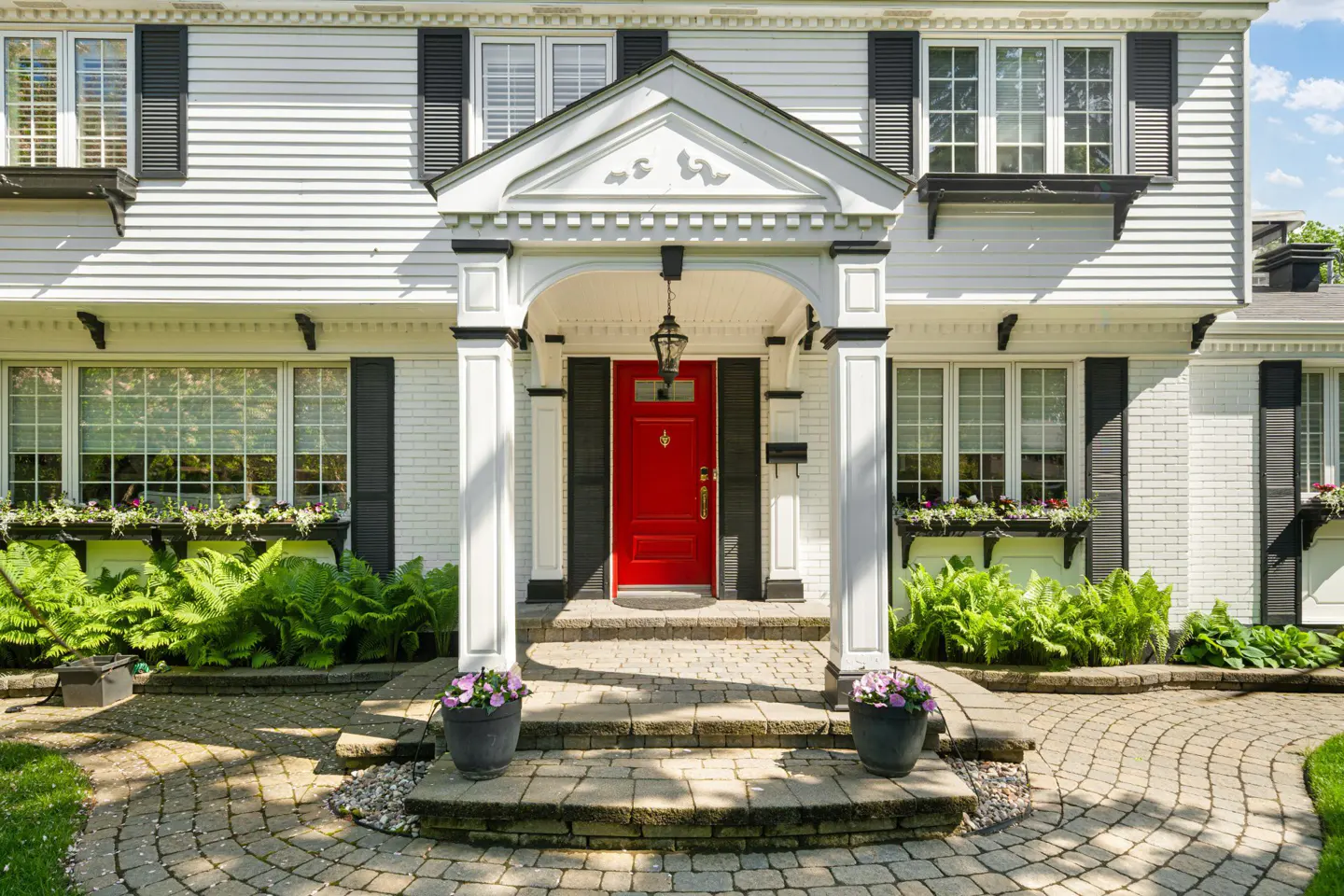 Exterior of a white house with black shutters and a bright red front door. A stone walkway leads to the entrance.