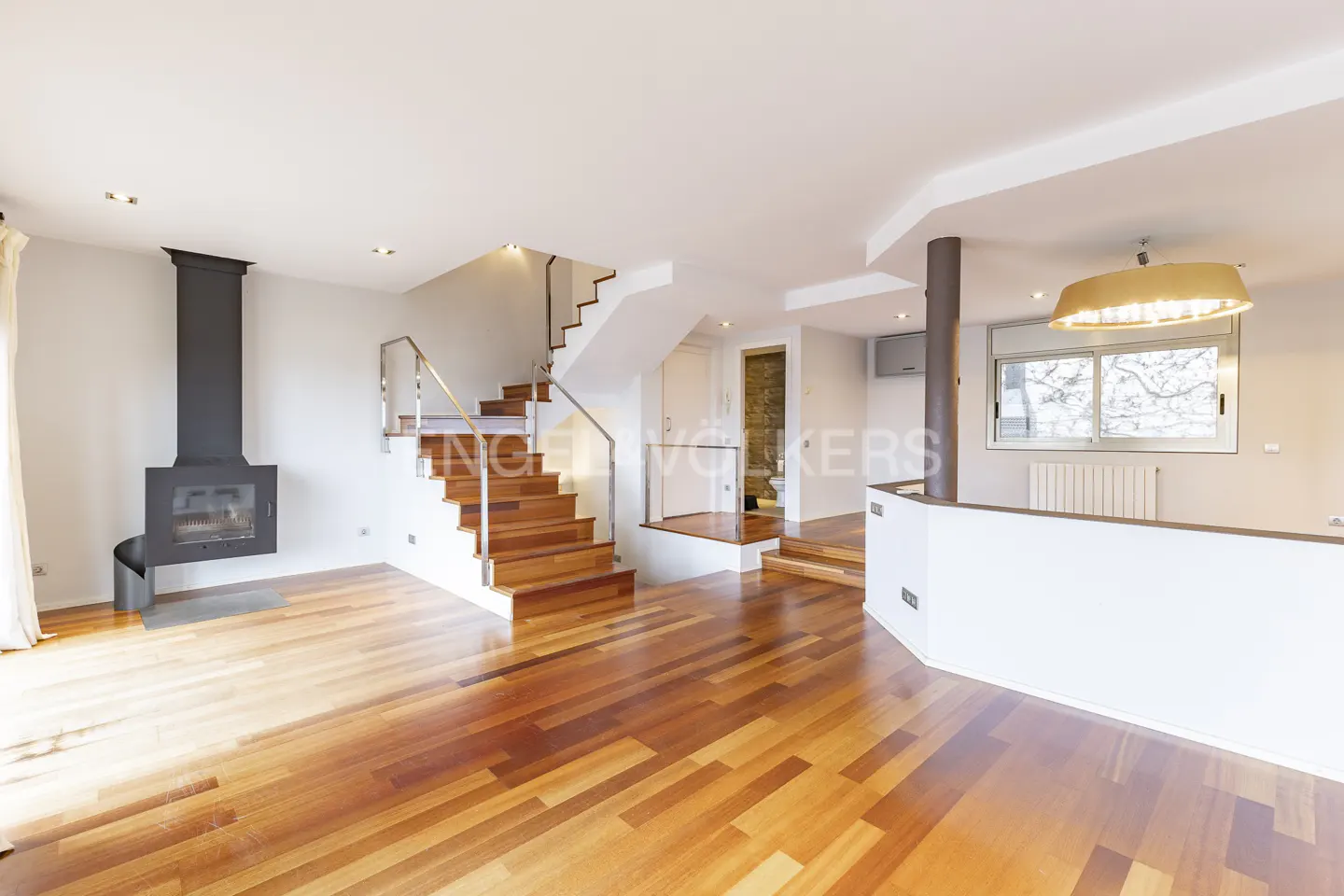 Open-plan living room with wood floors, a black fireplace, and a staircase with stainless steel railings.