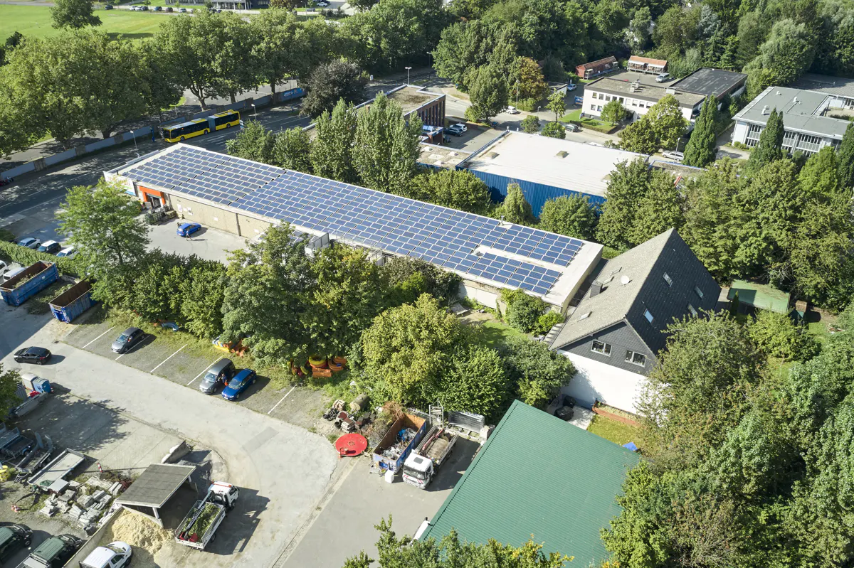 Aerial view of a commercial building with solar panels, surrounded by trees and parking lots.