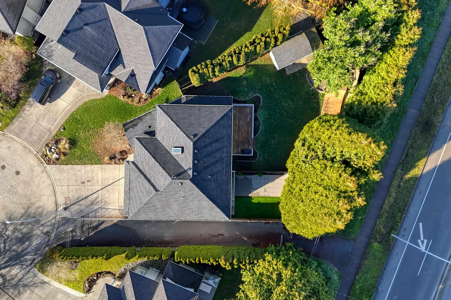 Aerial view of a house with a gray roof, green lawn, and trimmed hedges. A driveway leads to the street.
