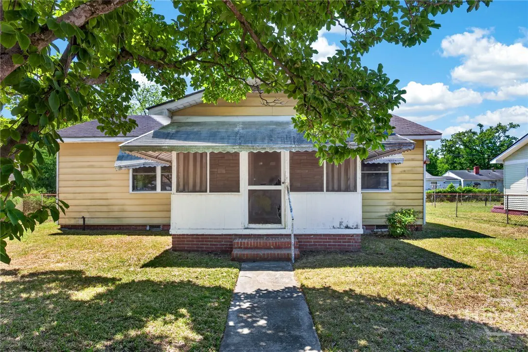 Exterior of a yellow, one-story house with a screened-in porch and a concrete walkway leading to the entrance.