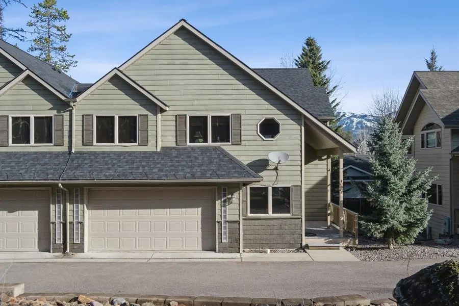 A two-story townhouse with a gray roof, light green siding, and a two-car garage on a sunny day.