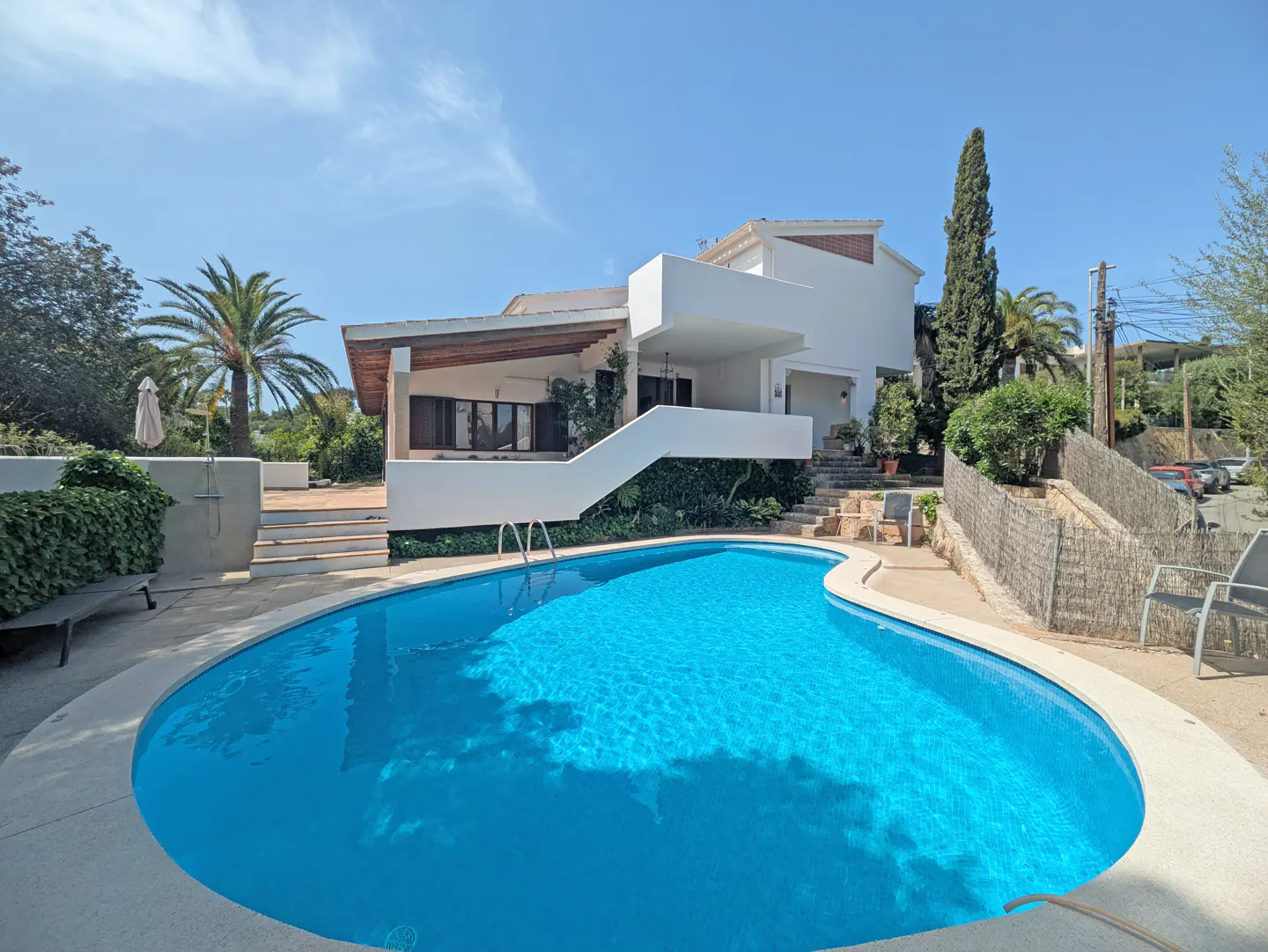 A kidney-shaped pool with blue water in front of a modern white house on a sunny day.