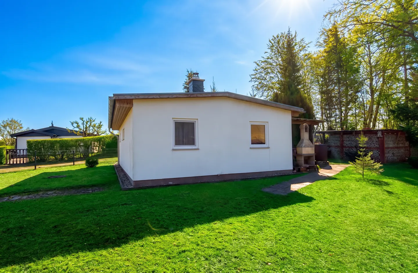 A small, white house with a chimney sits on a green lawn under a bright blue sky.