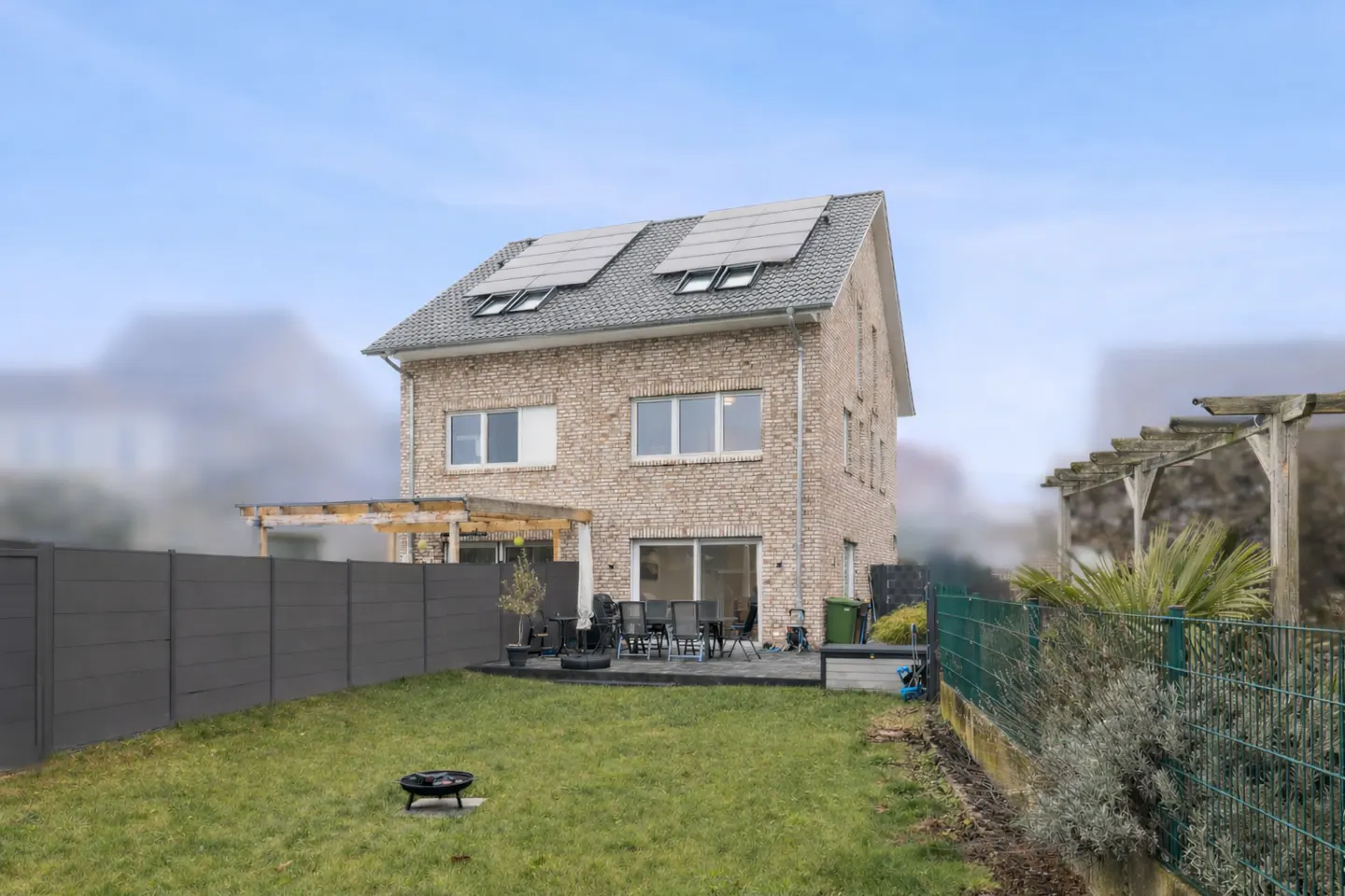 Backyard view of a two-story brick house with solar panels on the roof. A patio set sits outside the sliding glass door.
