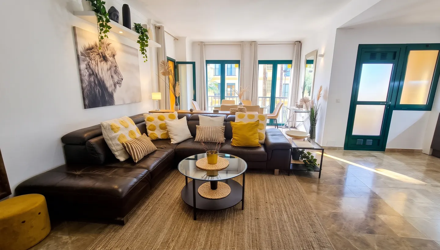 Modern living room with a dark leather sectional, yellow and white pillows, a glass coffee table, and a large lion print.