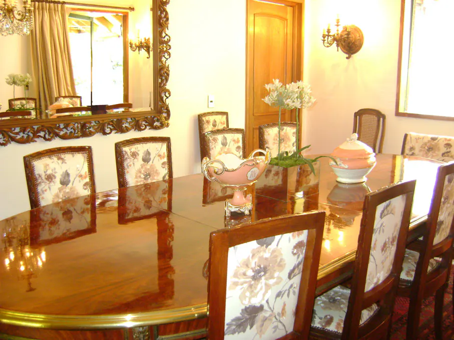 Formal dining room with a long, shiny wood table, floral upholstered chairs, and ornate mirror.