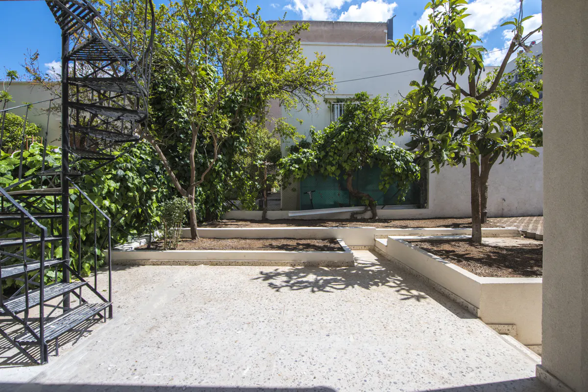 A bright courtyard with a black spiral staircase, trees, and a white building in the background.