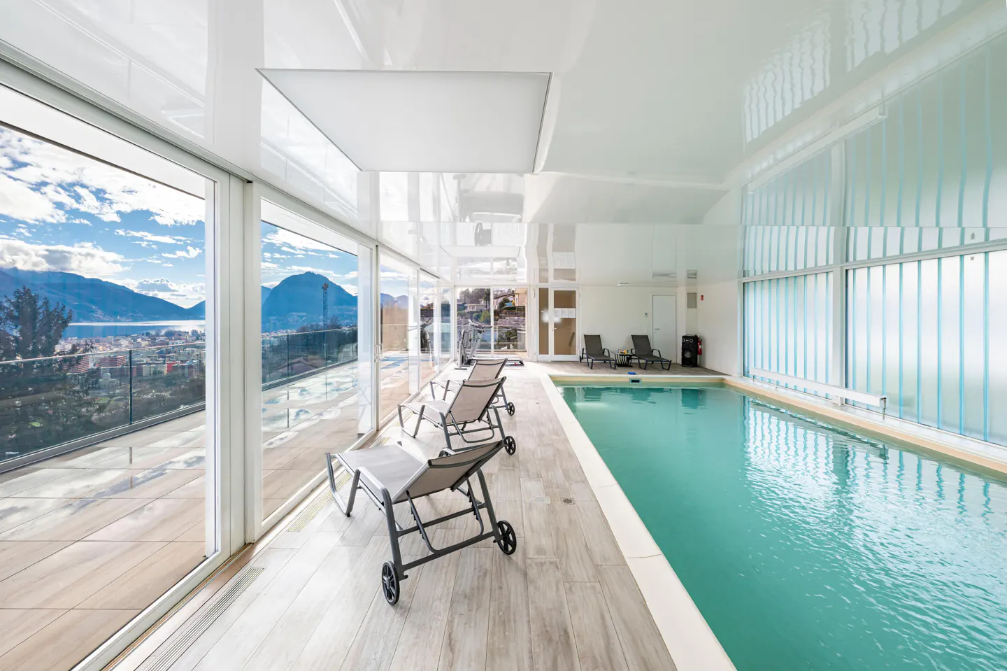 Indoor pool area with lounge chairs, light wood floors, and a large window with a mountain view.