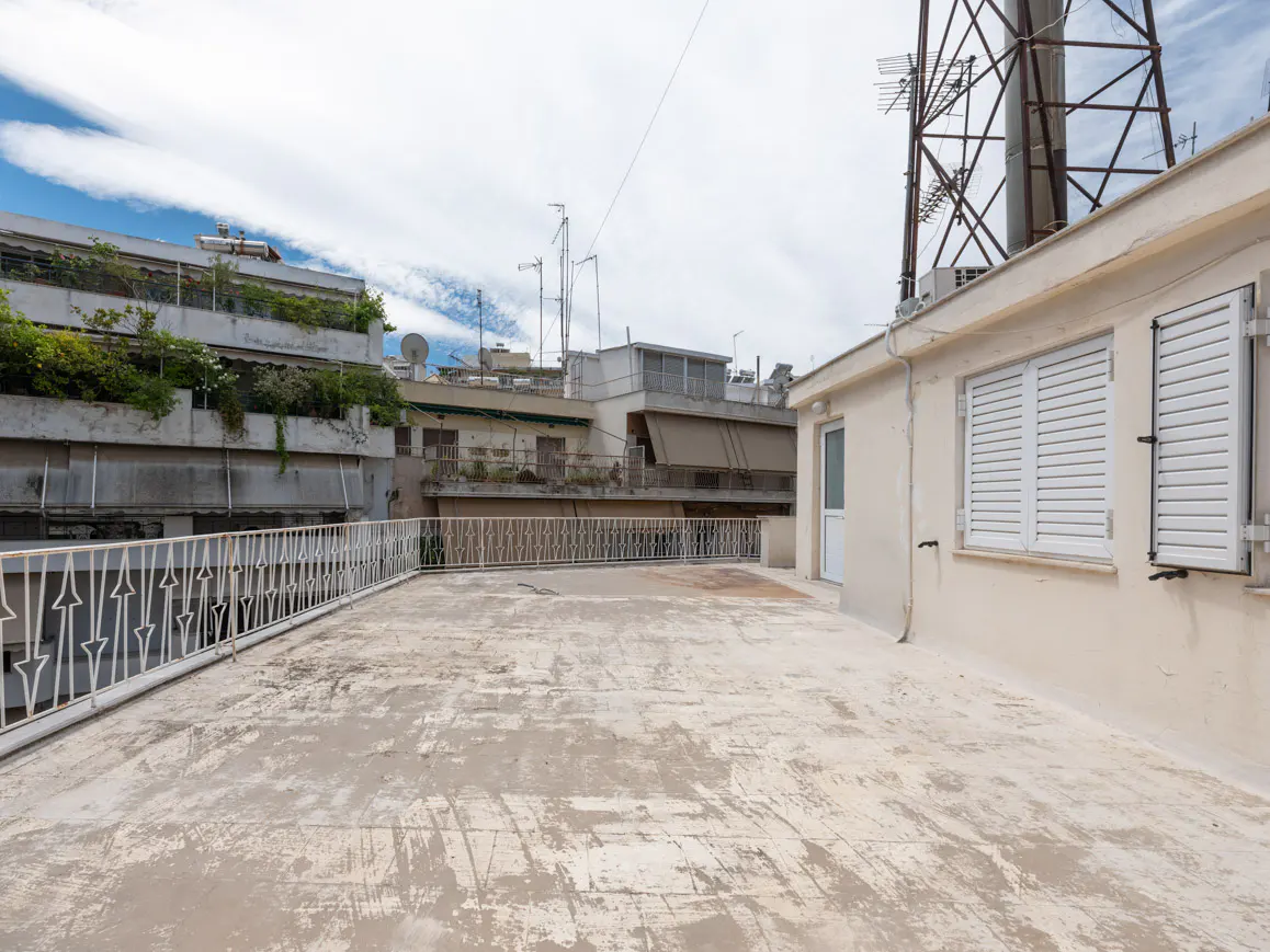 Spacious rooftop terrace with a white metal railing, beige exterior walls, and views of neighboring city buildings.