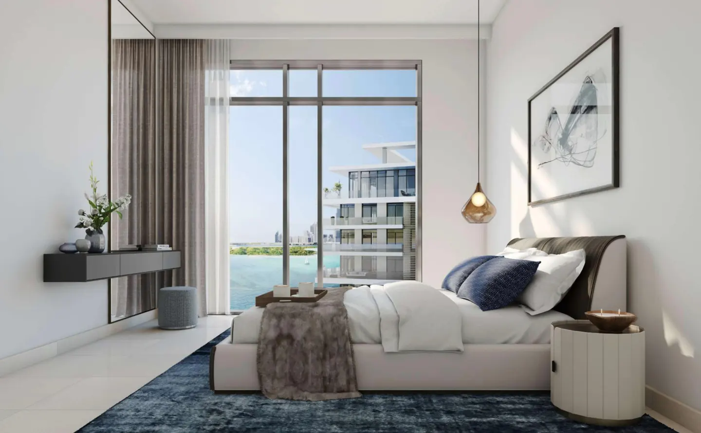 Bright bedroom with a large window view of the ocean. A bed with white linens and blue pillows sits on a blue rug. A gray console table is on the left.