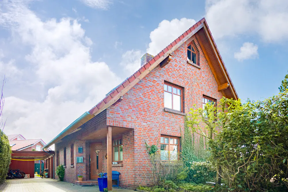 A two-story brick house with a gabled roof and a covered porch on a sunny day.