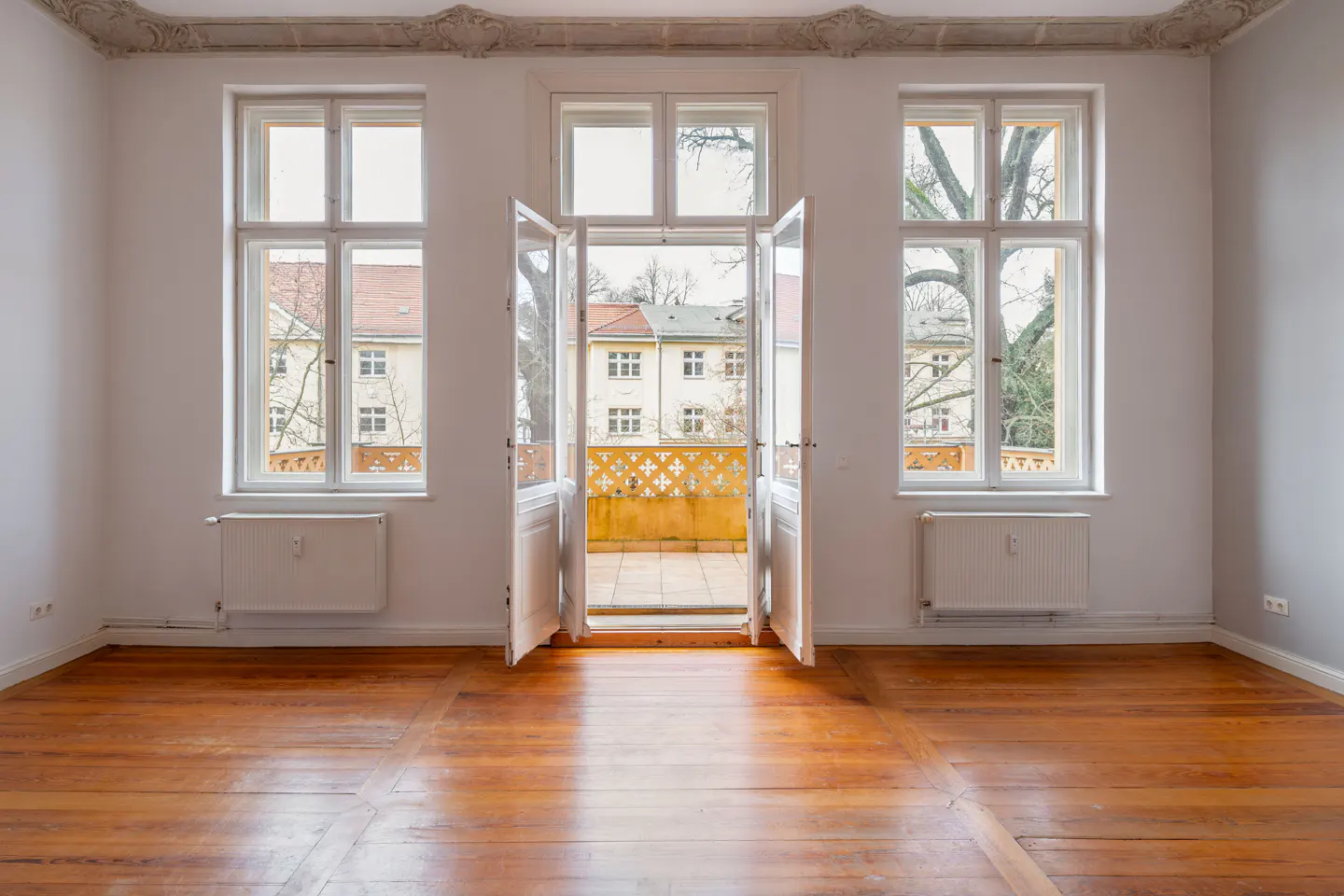 Empty white room with wood floors, three windows, and open doors to a balcony.