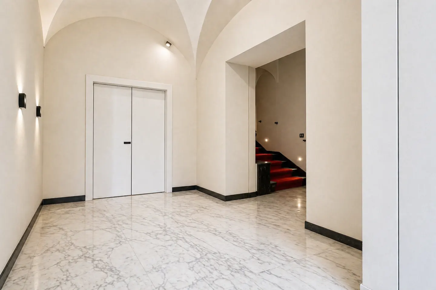 Minimalist hallway with white vaulted ceilings, marble floors, and a doorway leading to stairs with a red carpet runner.