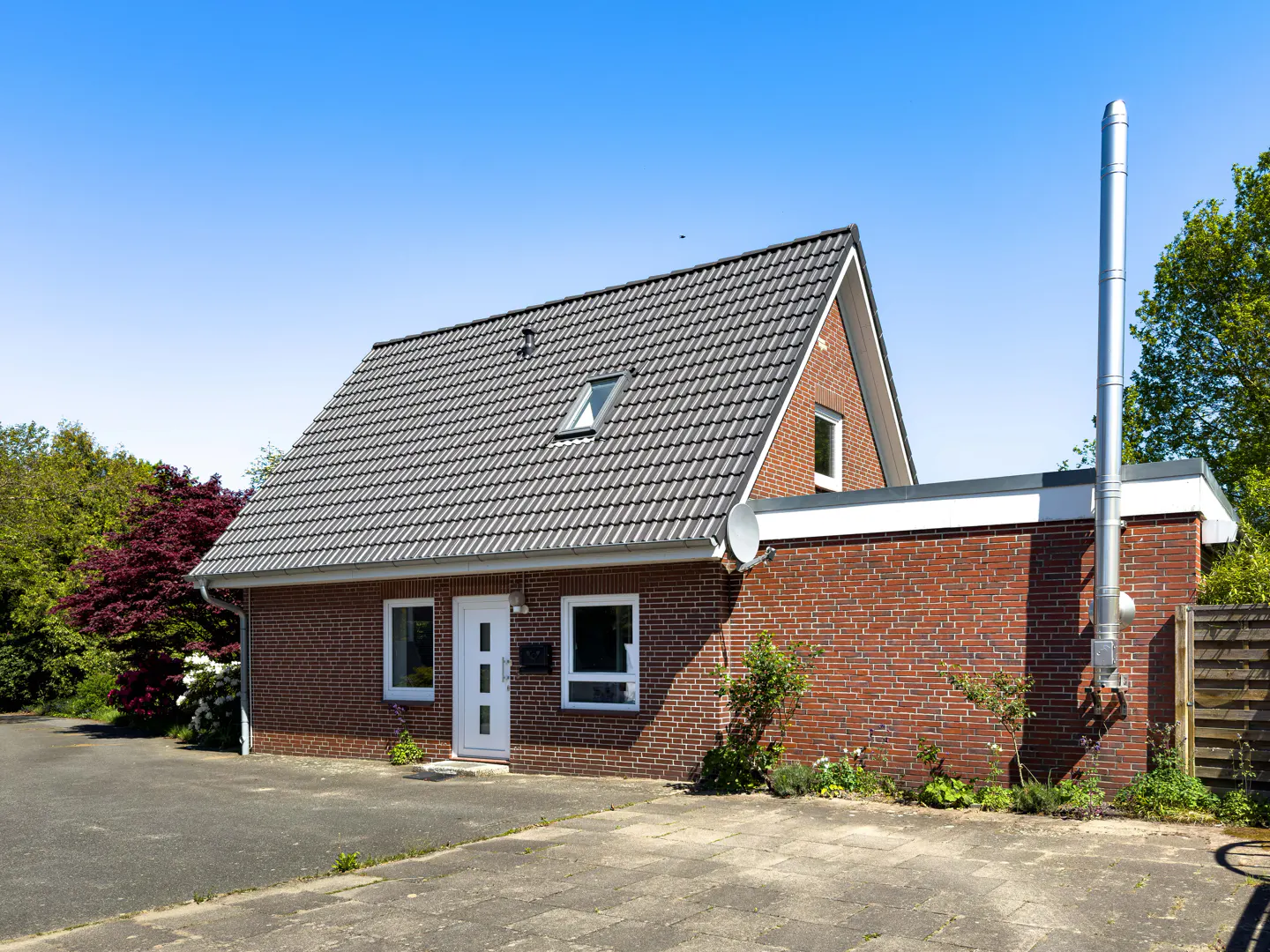 A single-story brick house with a gray tiled roof and a tall metal chimney under a clear blue sky.