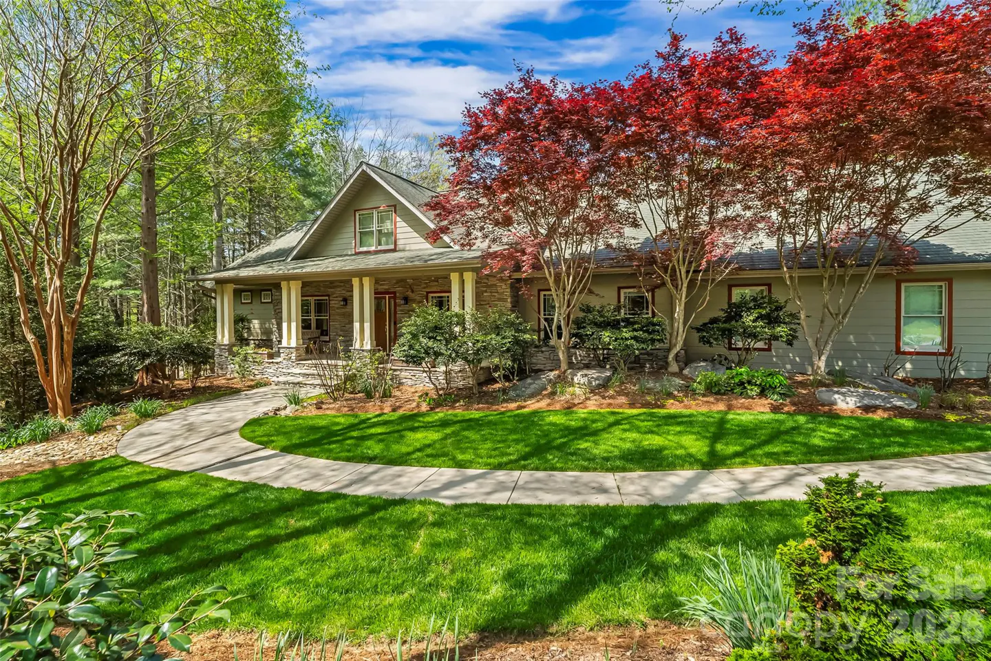 Exterior of a one-story house with a stone porch, green lawn, and red-leaved trees under a blue sky.