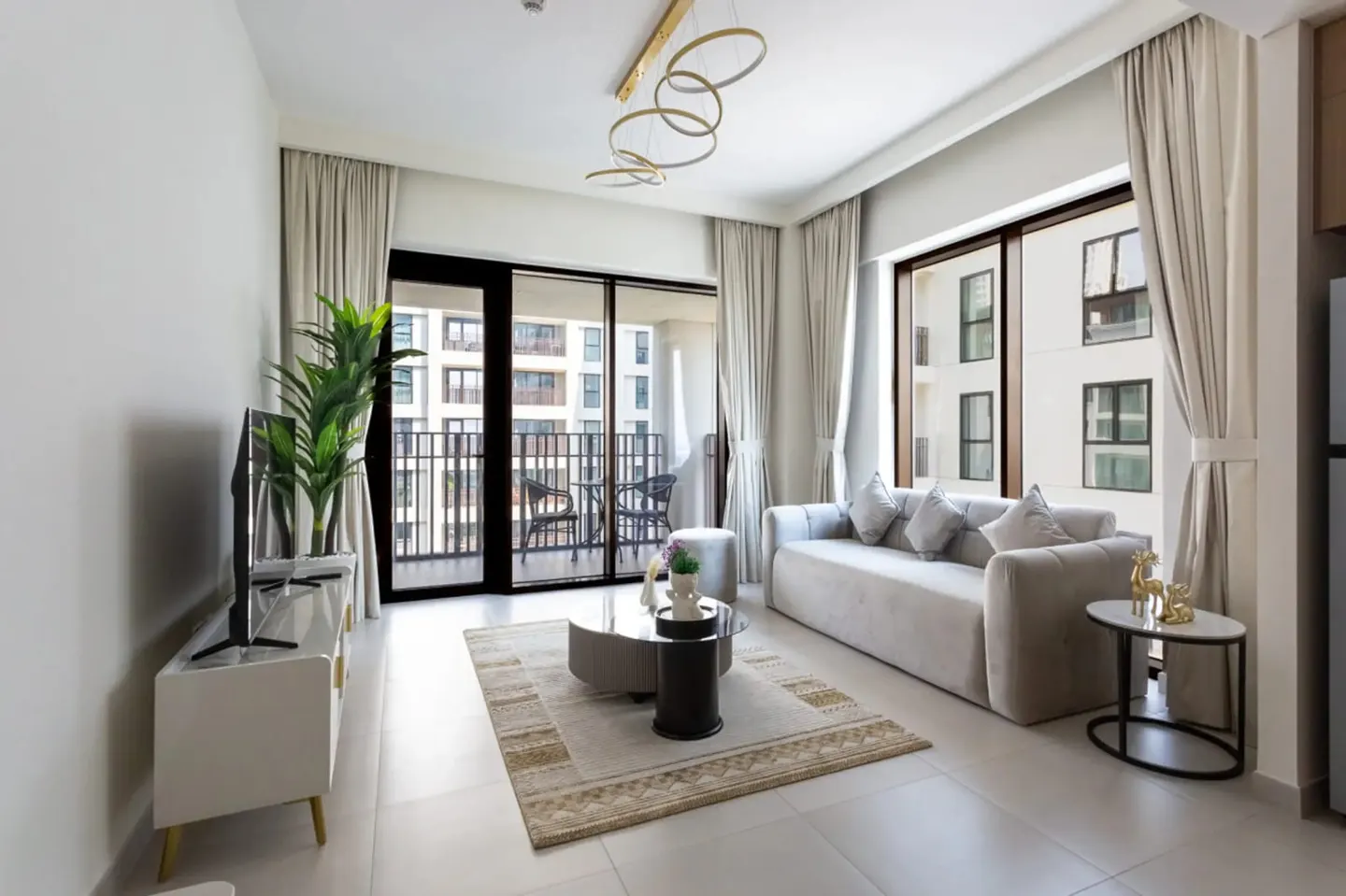 Living room with a gray sofa, round glass coffee table, and a balcony with a view of a building.