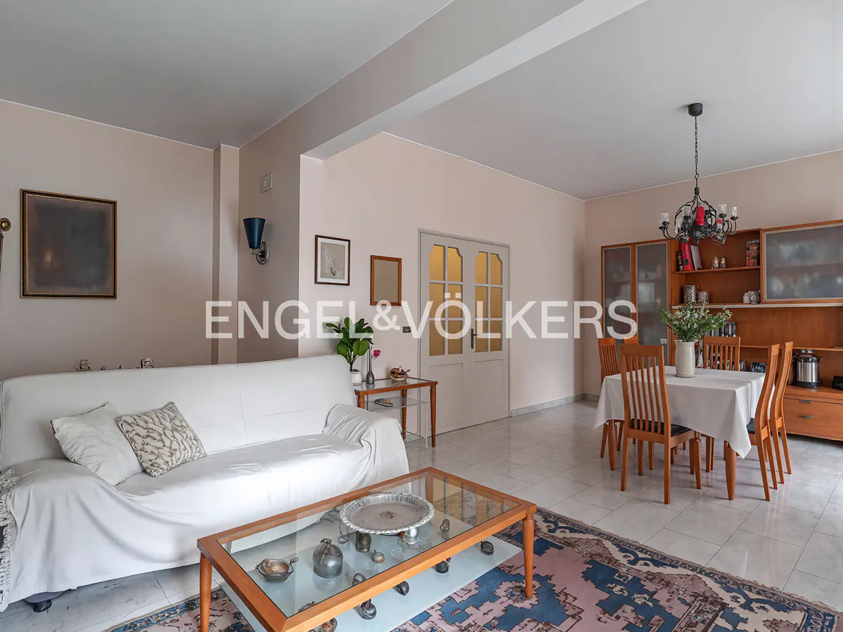 A living and dining area with a white sofa, glass coffee table, and wooden dining set under a chandelier.